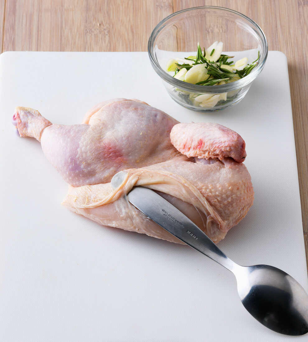 Skin of chicken being removed with spoon on chopping board