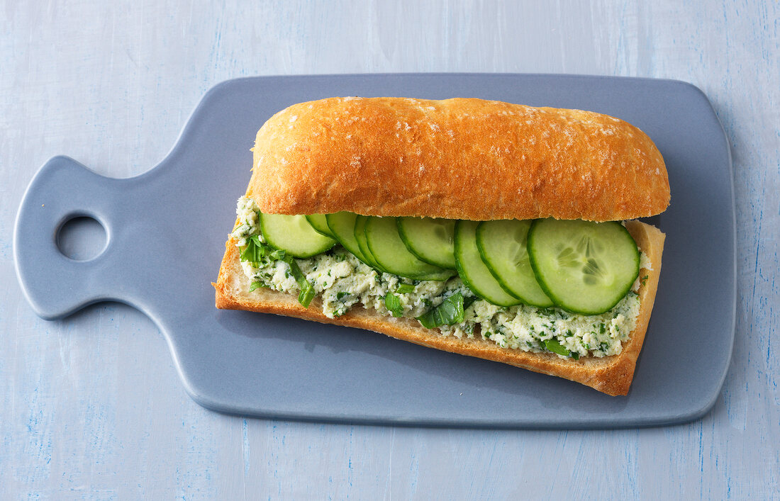 Chicken sandwich with cream and cucumber on chopping board