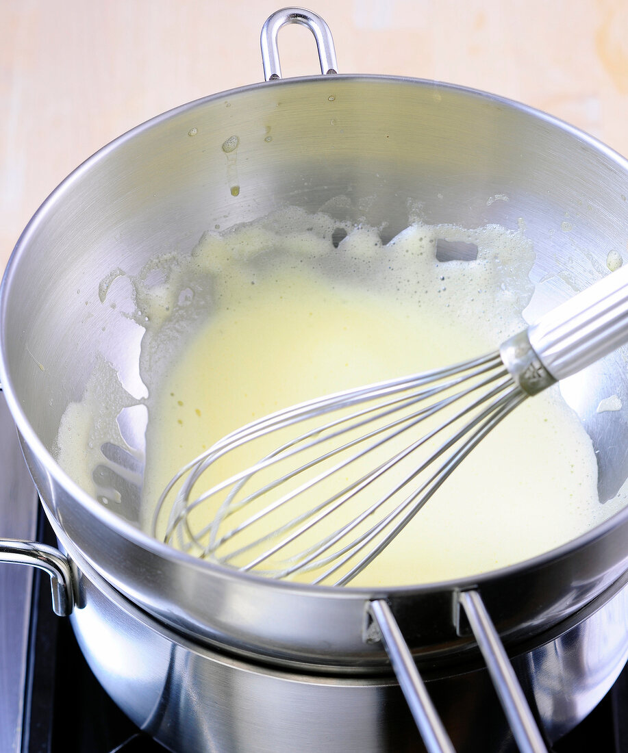 Close-up of whisked eggs with whisk in pan for preparation of hollandaise sauce, step 3