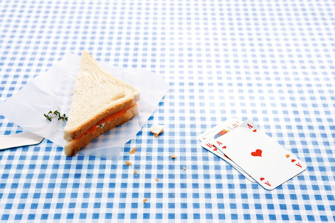 Sandwich and playing cards on blue checked blanket