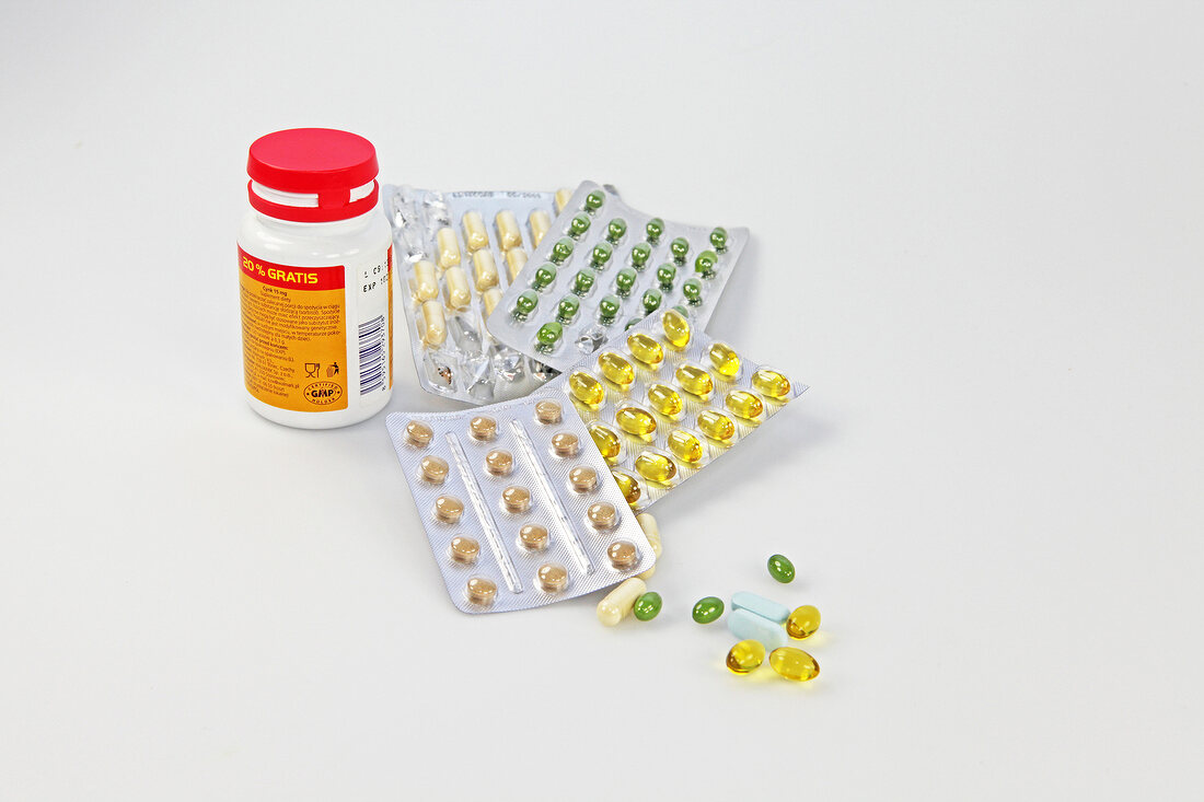 Multi-coloured pills in packets and bottle of pills on white background
