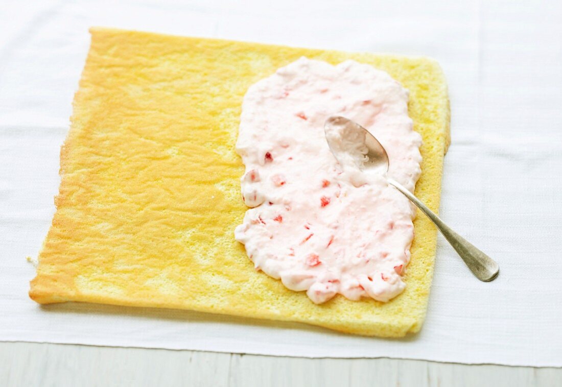 Swiss roll being made: strawberry cream being spread onto a sponge base