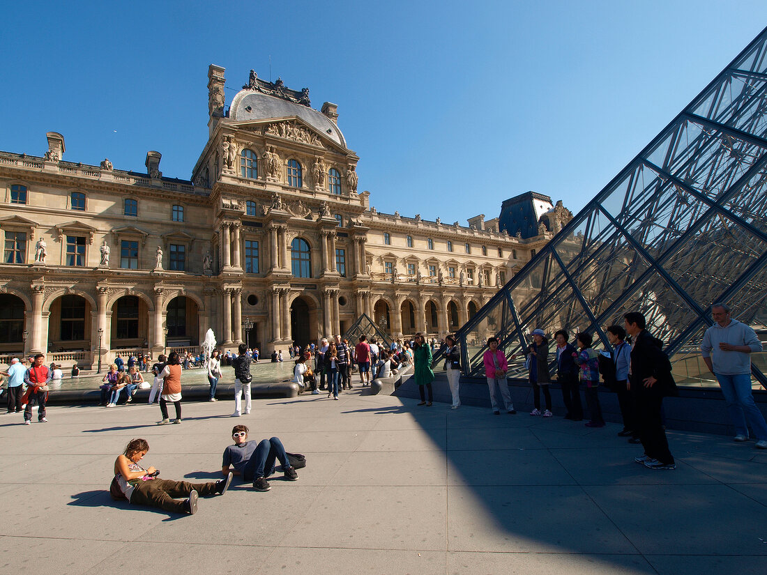 Tourists at Louvre pyramid facade in Paris, France