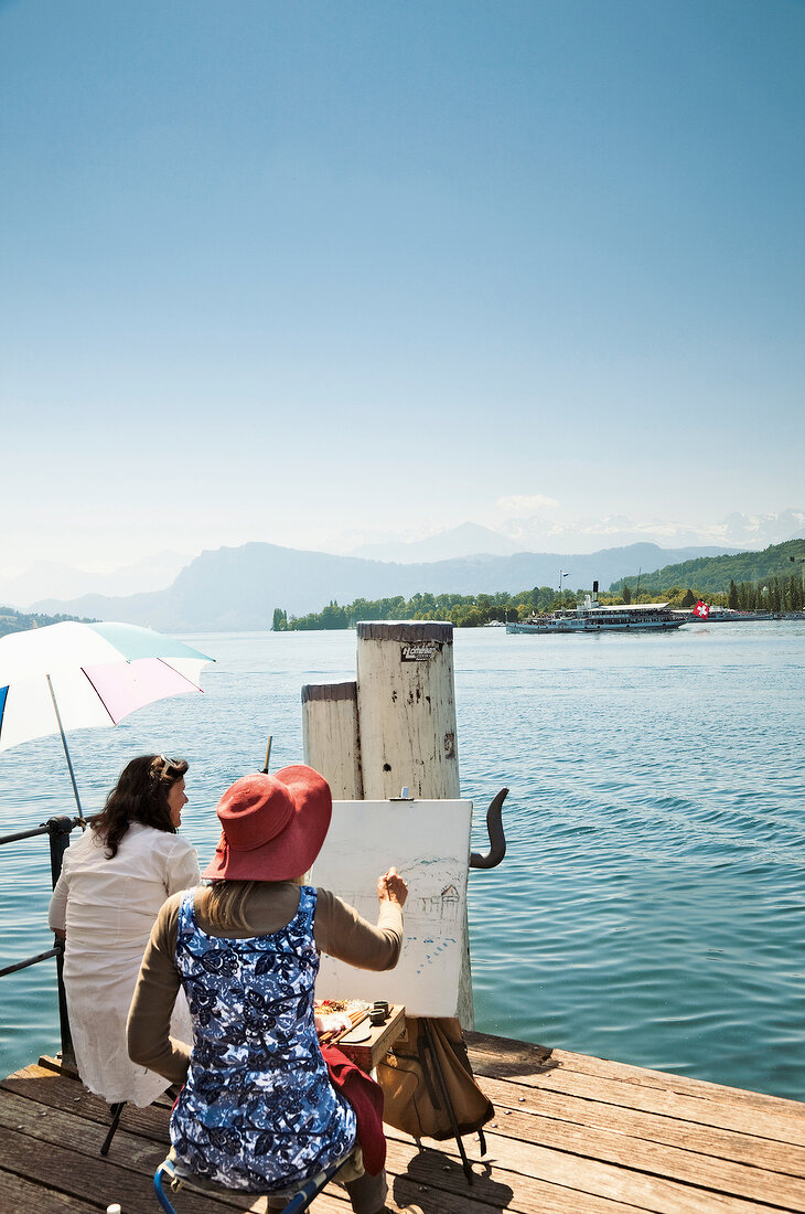 Rear view of artist painting the Lake Lucerne and the Alps on canvas, Lucerne, Switzerland