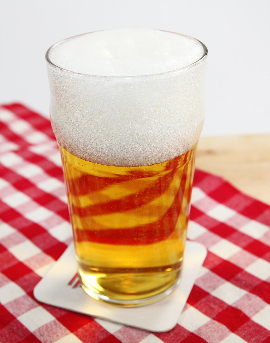 Glass of beer with froth on red and white checked table cloth