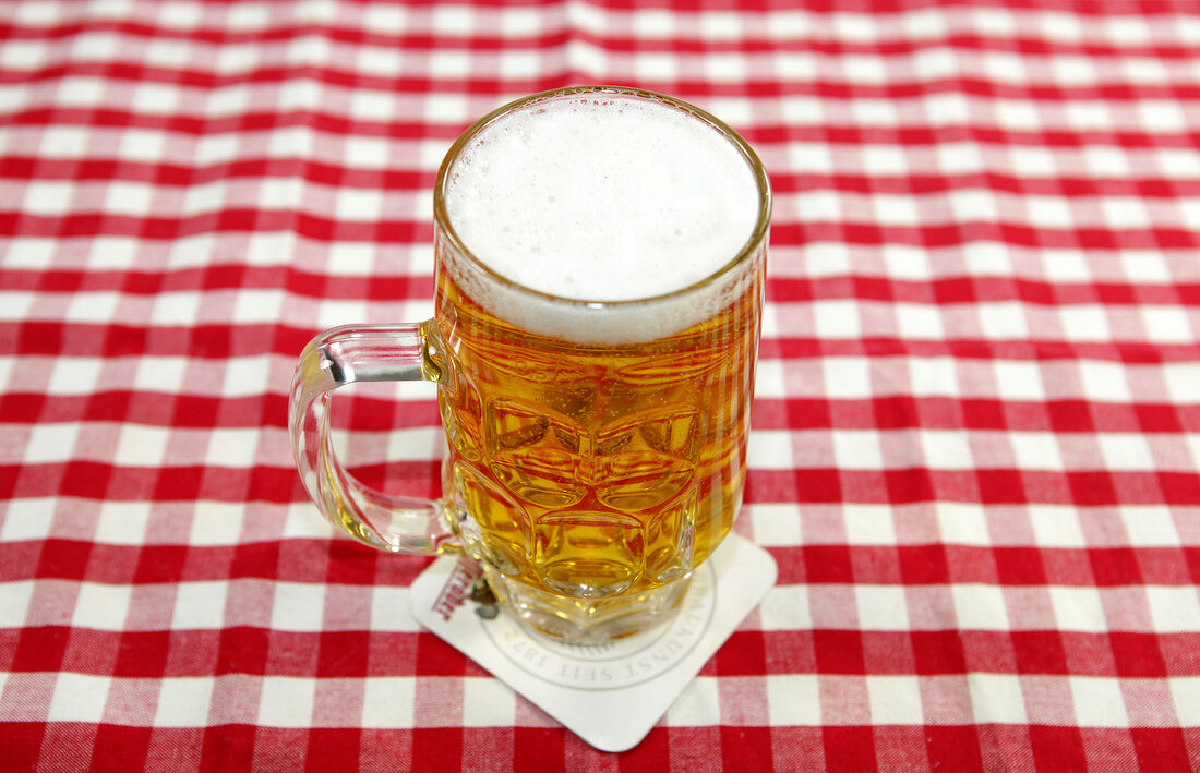 Bier in kleinem Glas auf Bierdeckel und rot-weiß karierter Tischdecke