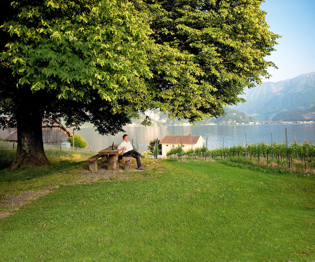 Toni Ottiger sitting on bench near Lake Lucerne and the Alps, Lucerne, Switzerland