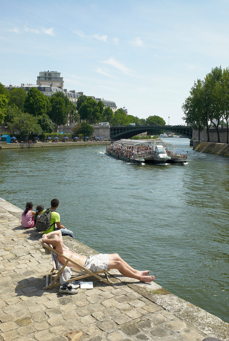 View of Seine river ship and people sitting on promenade, Paris, France