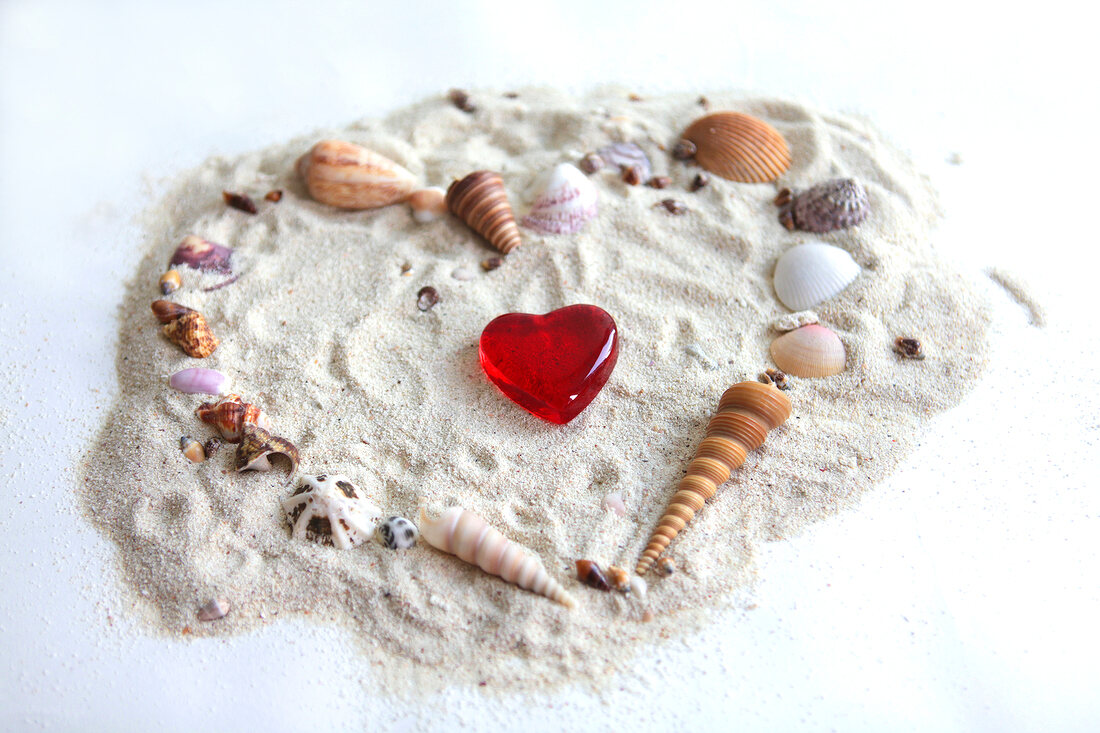 Rotes Herz umrandet von einem Herz aus Muscheln im Sand