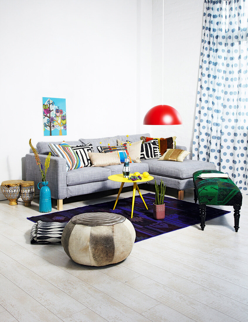 Ethno style living room with ottoman, gray sofa, cushion and colourful accessories