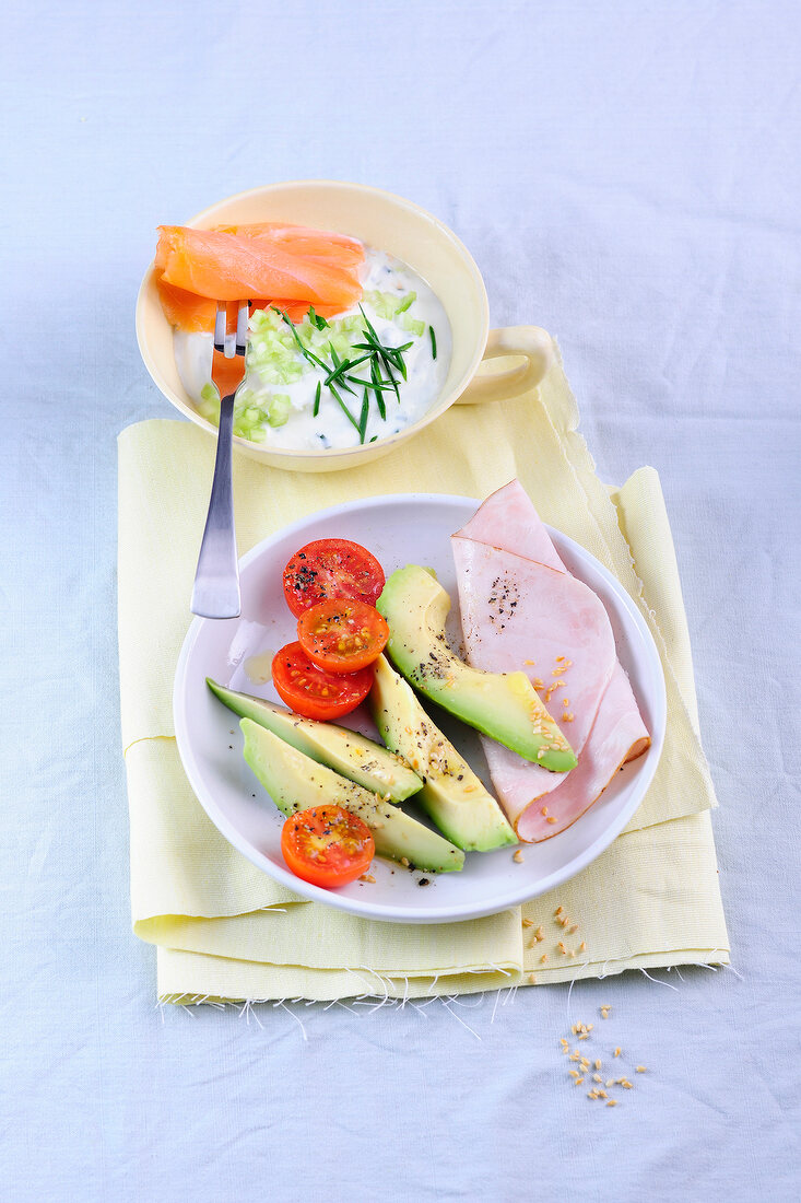 Bowl of cucumbers curd with salmon, avocado with turkey breast on plate, low GI diet food