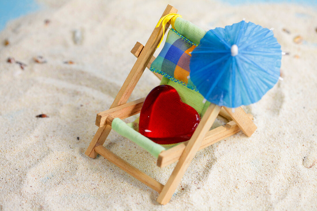 Red heart shaped stone in small deck chair with parasol in sand