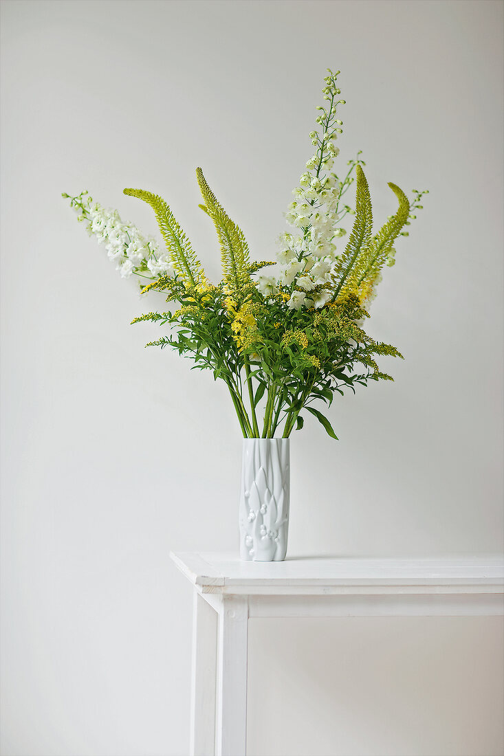 Tall vase with yellow and white flowers on white table