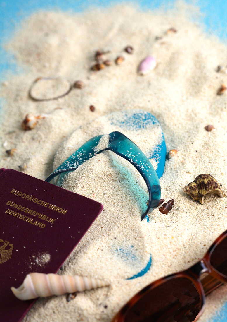 Flip Flop und Reisepass im Sand mit Muscheln und Sonnenbrille