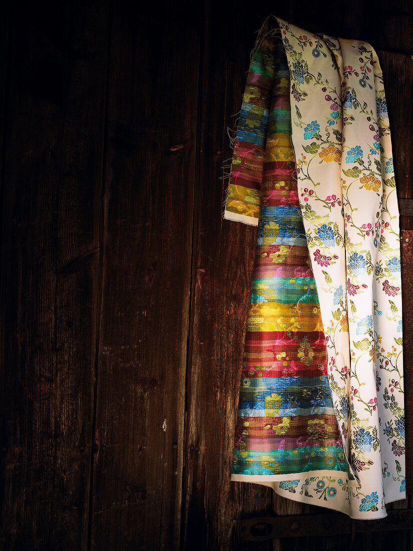 Colourful fabric with floral pattern hanging in front of wooden wall