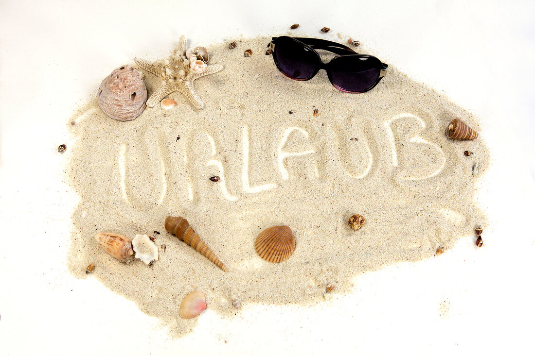 "Urlaub" im Sand geschrieben mit Mu scheln drum herum und Sonnenbrille