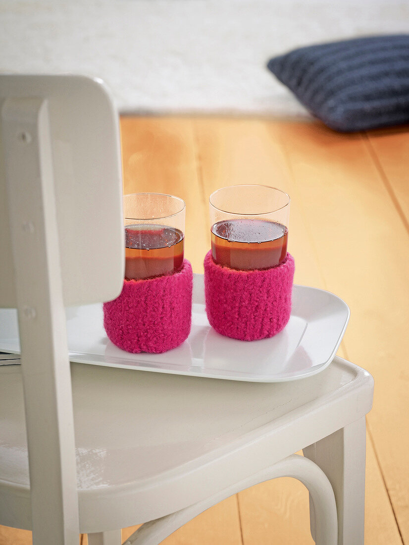 Two tea glasses with woollen cup covers on chair