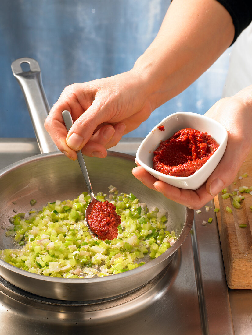 Close-up of hand adding tomato paste in pan with vegetables, step 1