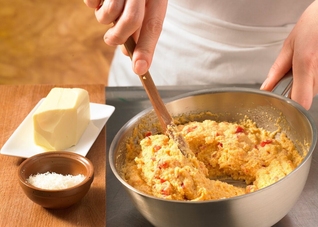 Close-up of hand stirring mixture for preparation of Peperonata and polenta