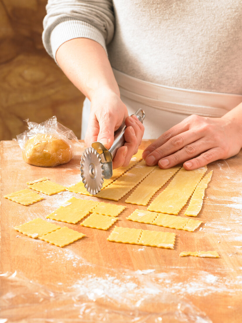 Close-up of hand cutting dough in shape for preparation of noodles