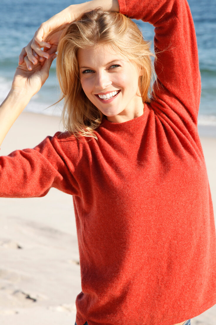 blonde Frau in orangefarbenem Pulli am Strand