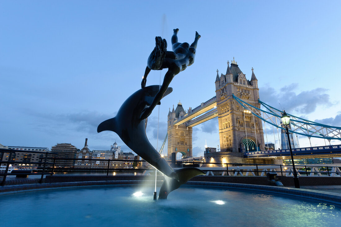 Sculpture of dolphin with girl and Tower Bridge in background at Southwark, London, UK