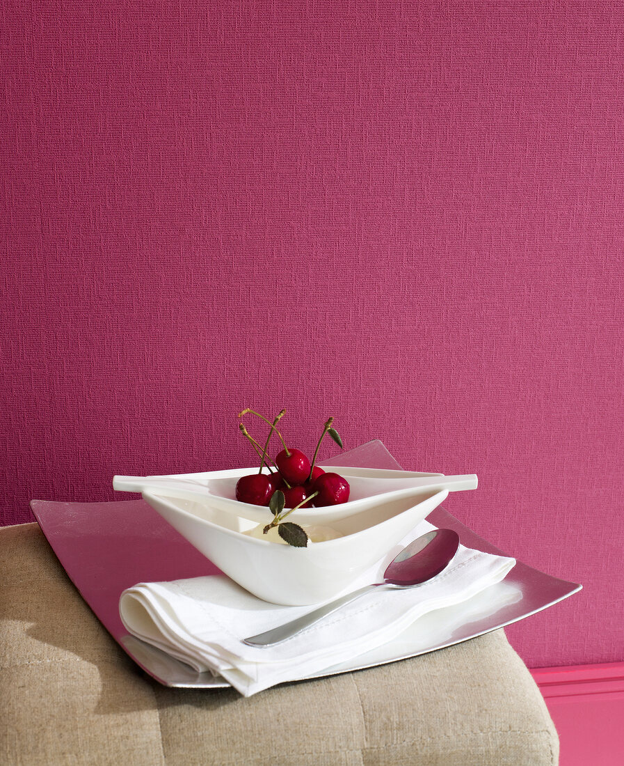 Close-up of tray with cherries, napkin and spoon against pink wall