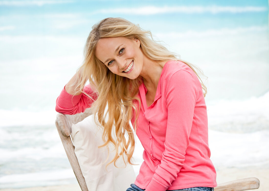 Portrait of happy blonde woman wearing pink sweater relaxing on chair and smiling