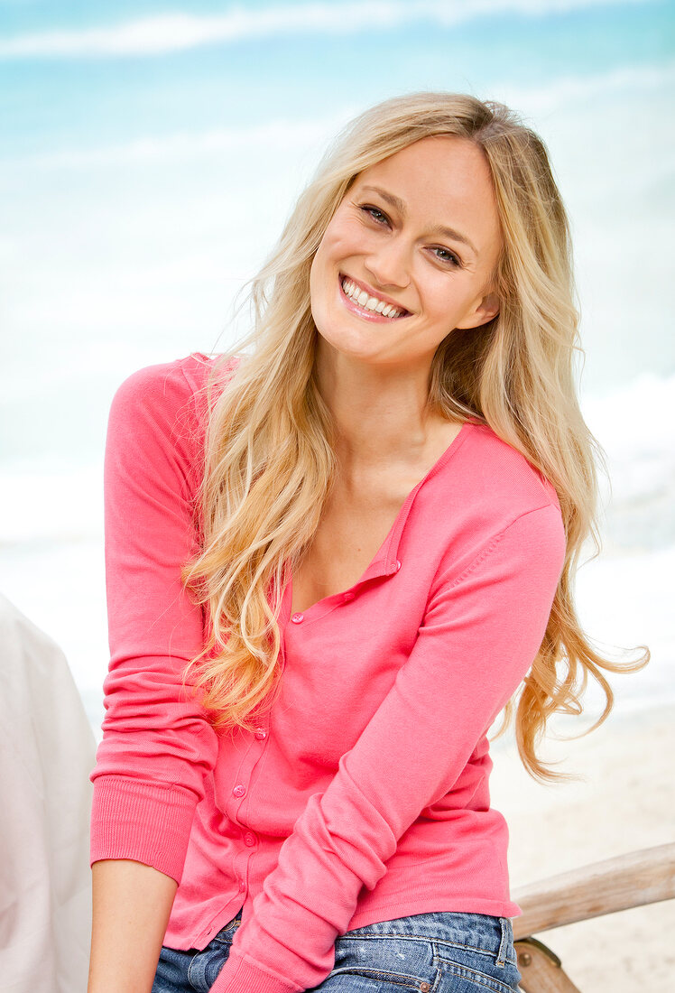 Portrait of happy blonde woman wearing pink sweater smiling on beach