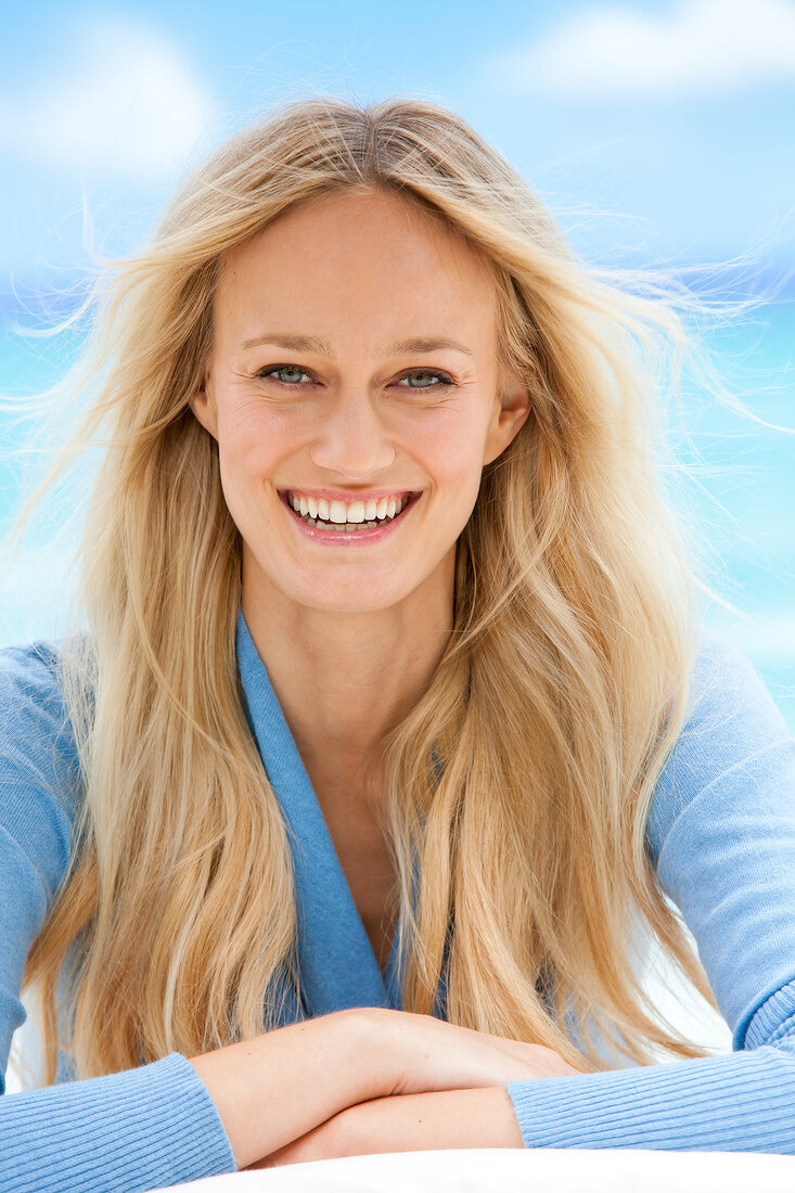 Close-up of happy blonde woman wearing blue sweater smiling with her arms crossed