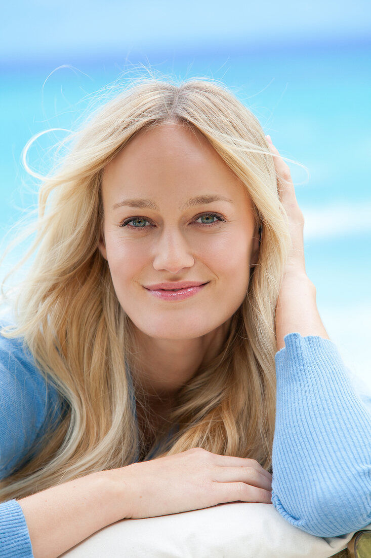 Portrait of beautiful blonde woman wearing blue sweater, smiling with hand in her hair