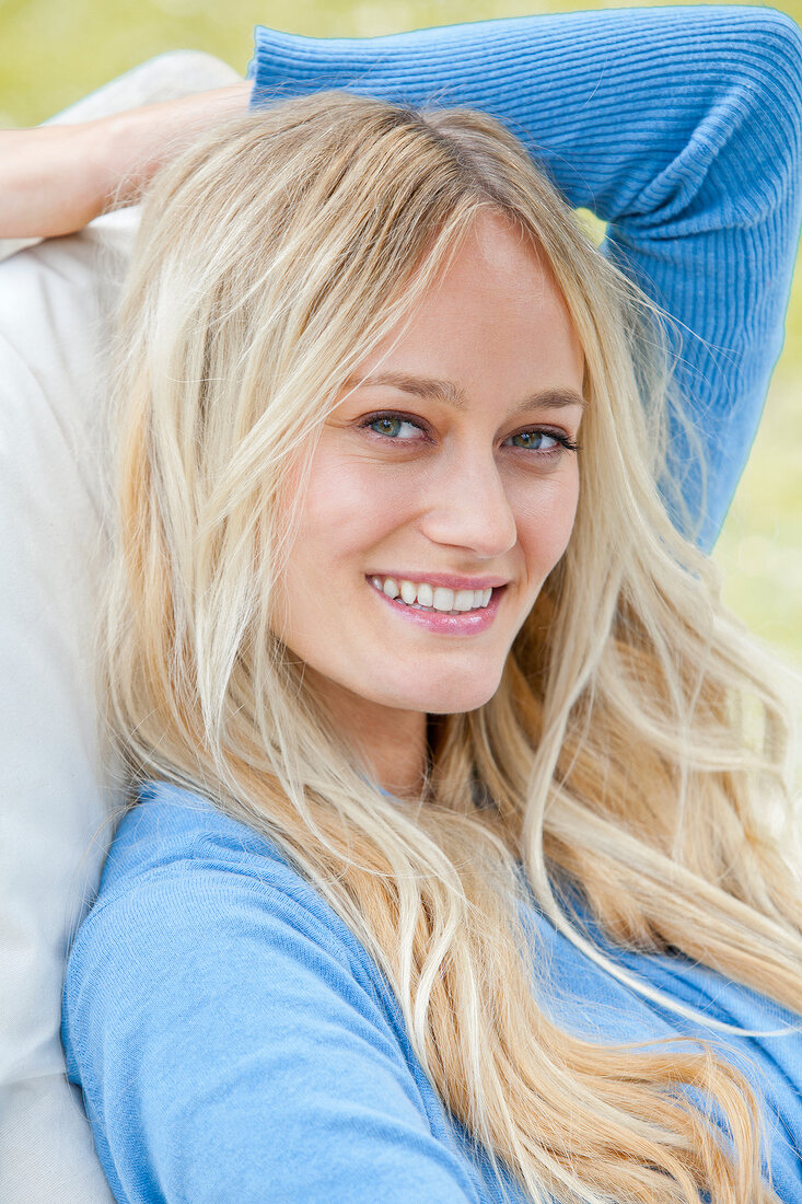 Portrait of beautiful blonde woman with long hair in blue sweater, sitting and smiling