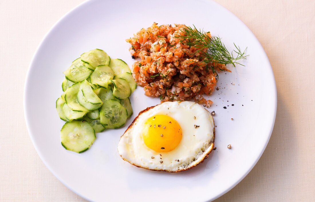 Salmon tartare with fried egg and cucumber on plate