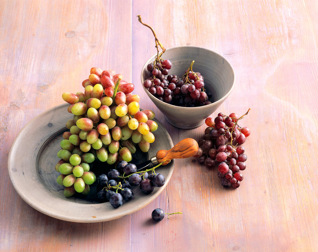 Different types of wine grapes in bowl and on plate 