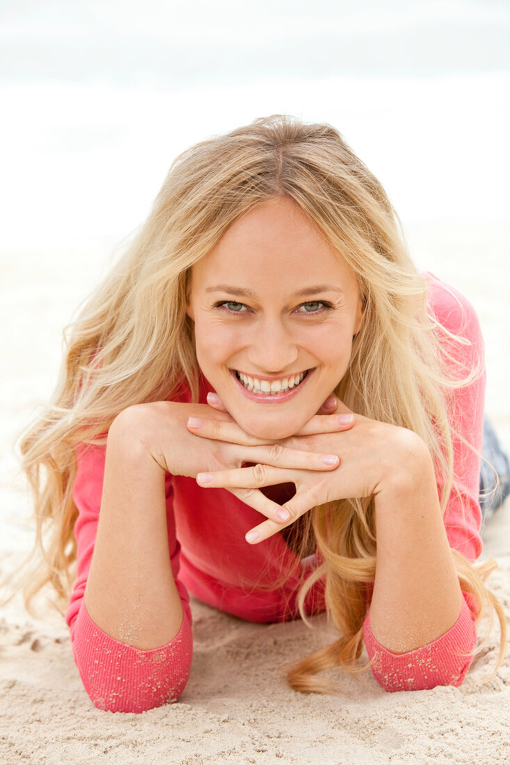Portrait of beautiful blonde woman in pink sweater lying with hands on chin, smiling