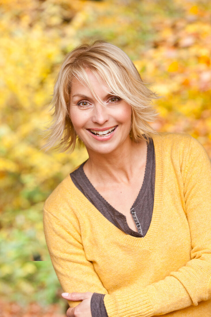 Portrait of happy woman wearing yellow sweater with arms crossed, smiling