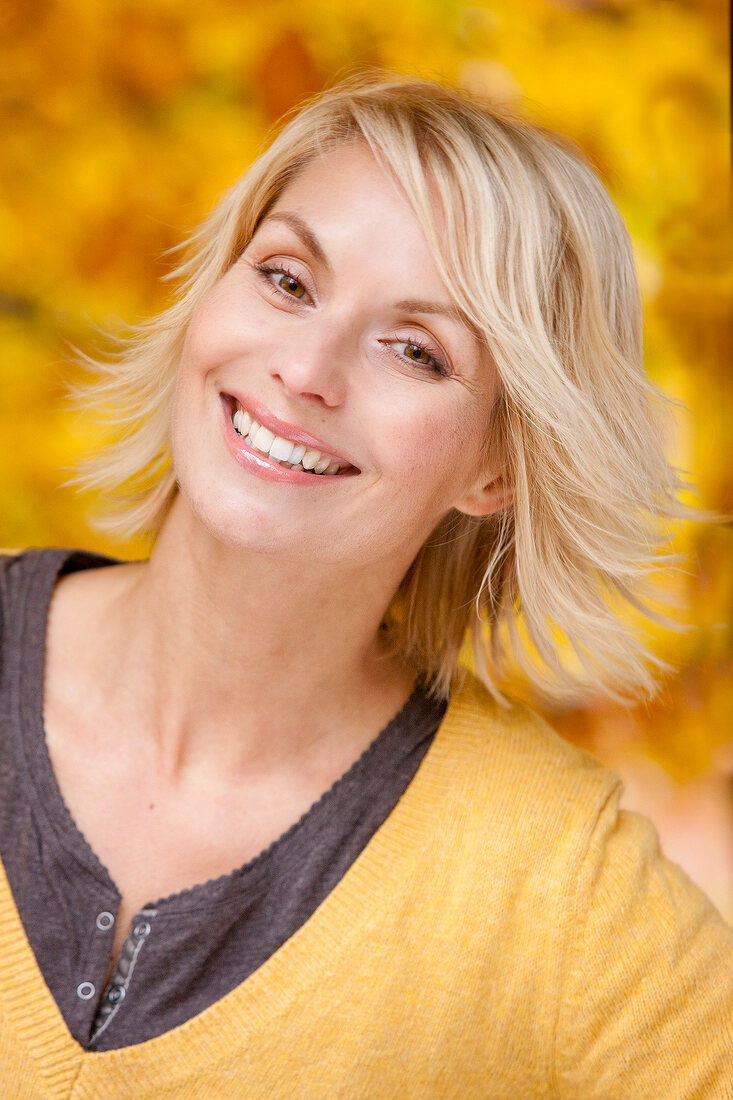 Portrait of happy blonde woman wearing yellow sweater smiling with head slightly tilted