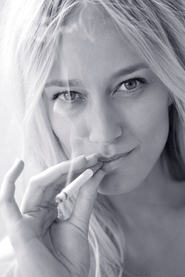 Close-up of beautiful woman with blonde hair smoking cigarette, black and white