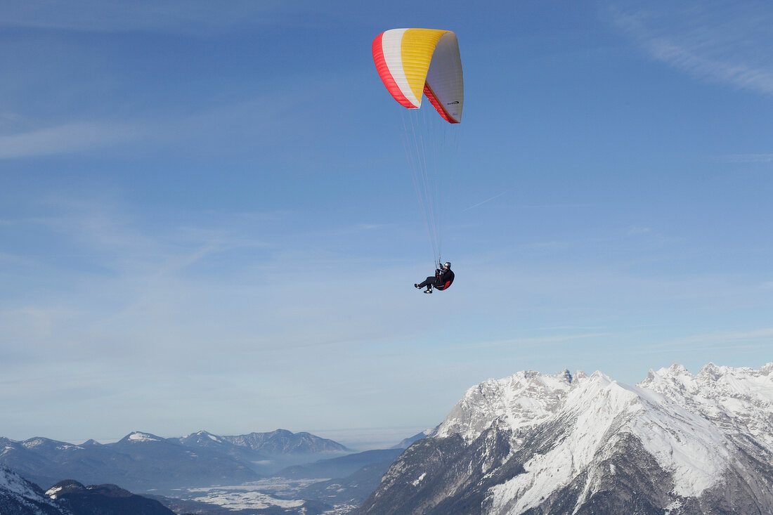 Man paragliding between snow mountains at Leutaschtal, North Tyrol, Italy