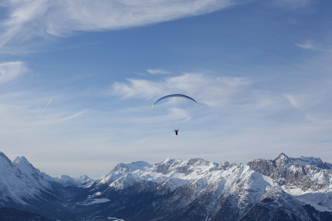 Man paragliding between snow mountains at Leutaschtal, North Tyrol, Italy