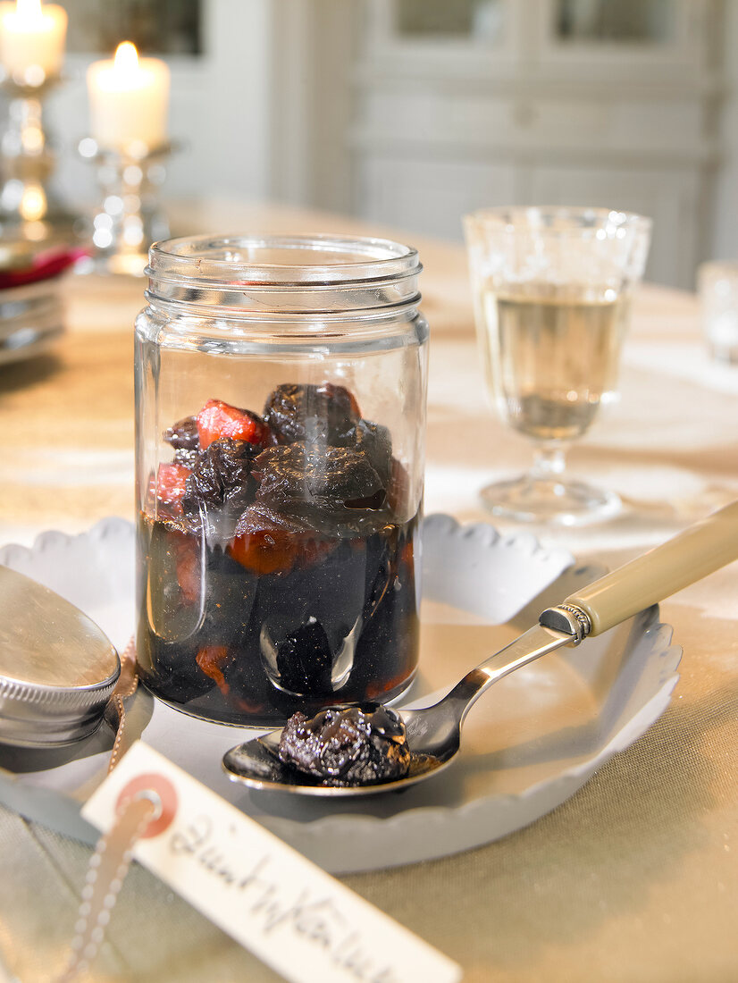 Glass with pickled prunes and spoon on tray