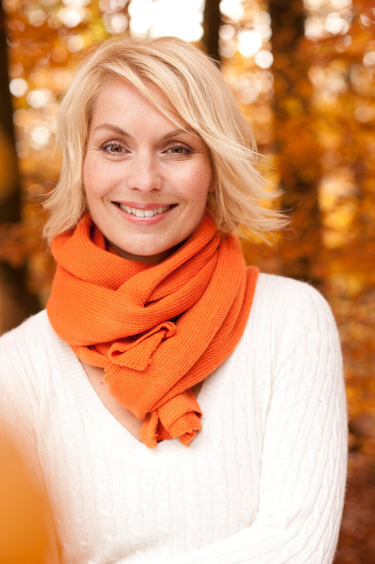 Portrait of blonde woman wearing white sweater and orange scarf, smiling