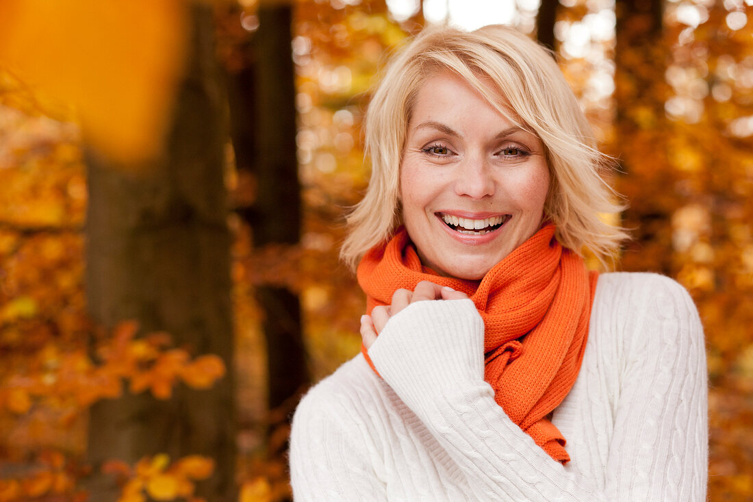 Pretty blonde woman with short hair wearing white sweater, smiling in autumn forest