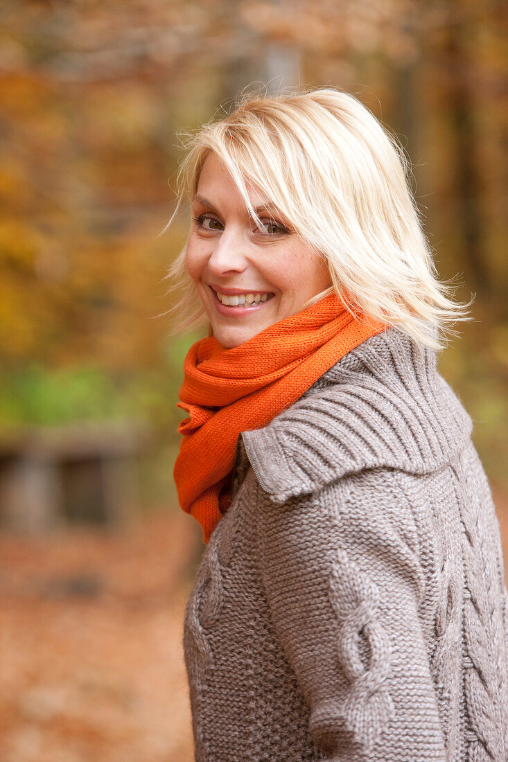 Pretty blonde woman wearing gray sweater and orange scarf looking over shoulder, smiling