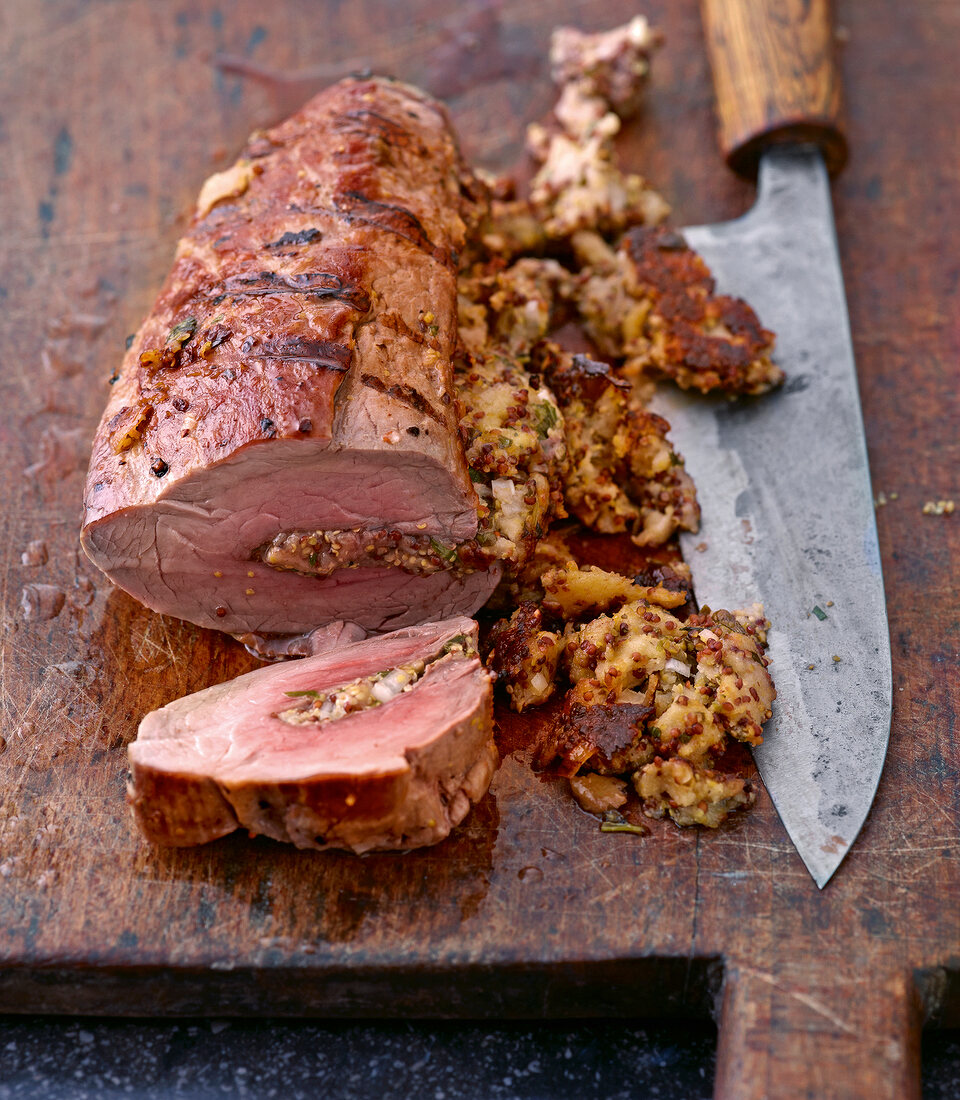 Close-up of stuffed pork with knife on wooden platter with knife