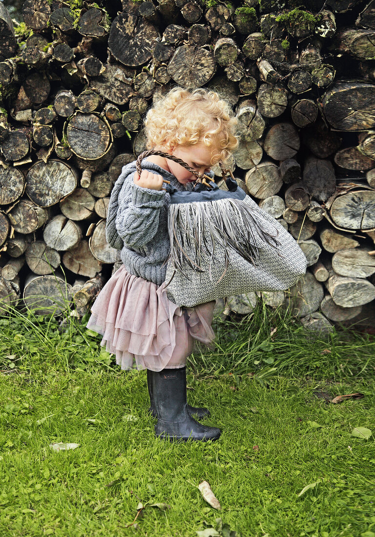 Small girl with curly hair wearing skirt and rubber boots looking into bag