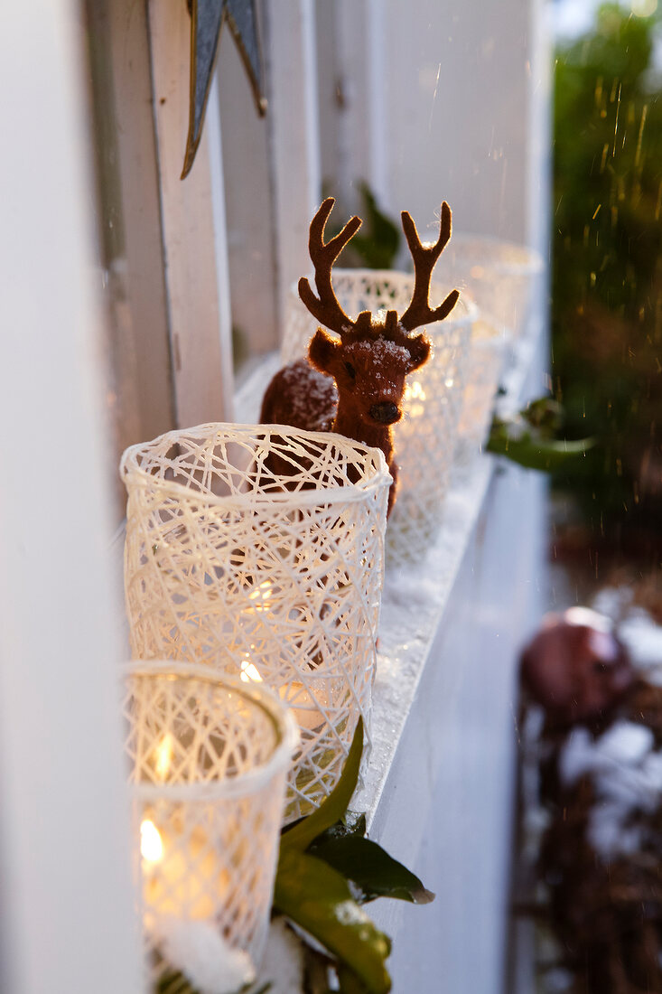 Close-up of window sill with lit candle in lanterns and deer figure