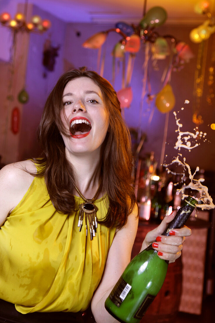 Portrait of happy woman wearing yellow top celebrating New Year's with champagne, smiling