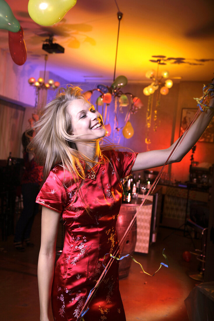 Frau im roten Satinkleid feiert und tanzt auf einer Silvesterparty