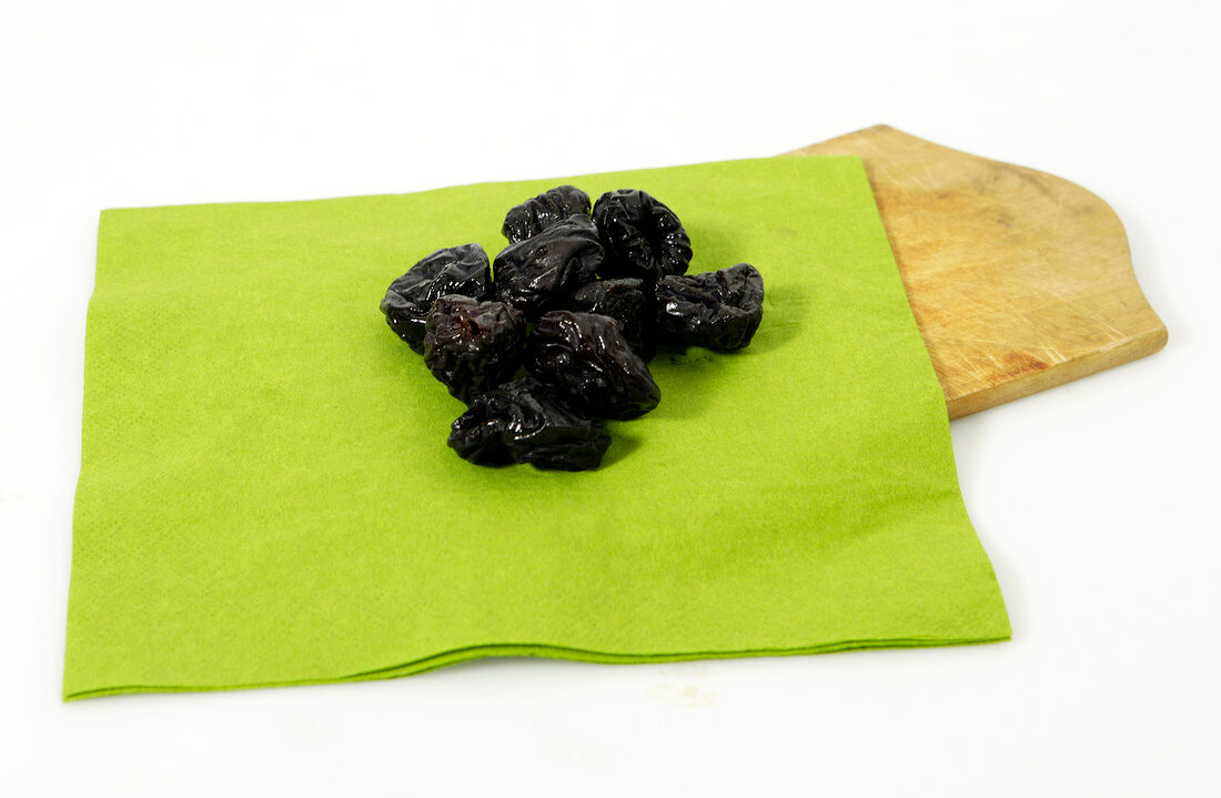 Dry plums on green cloth with wooden platter on white background